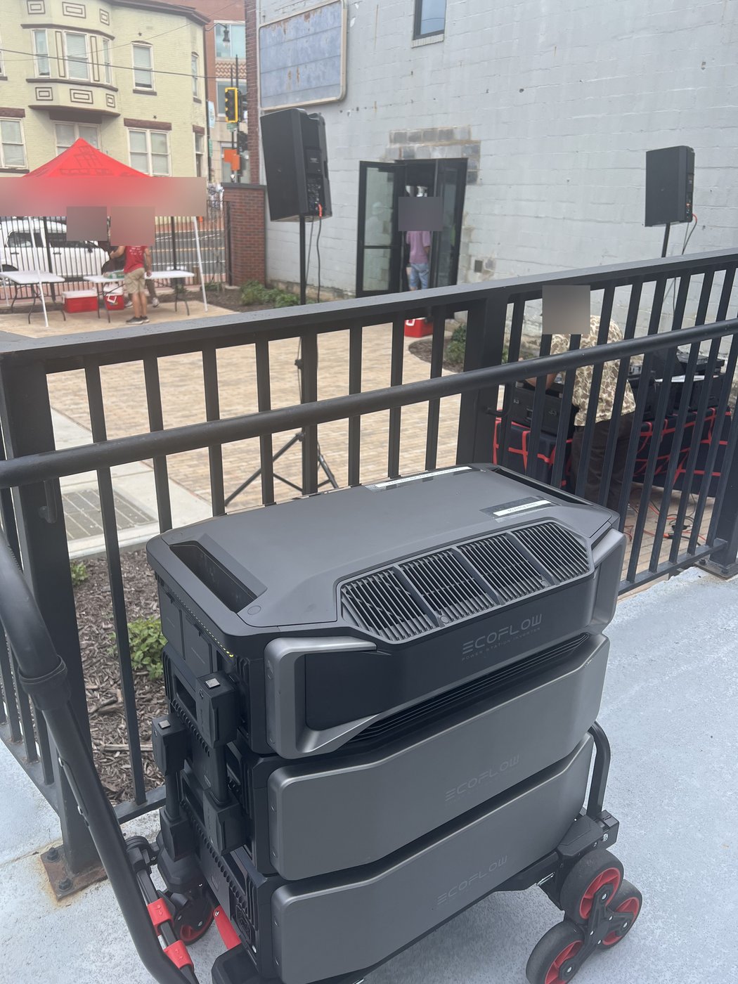 EcoFlow rig on its cart beside a plaza railing, powering a pair of PA speakers at a street event