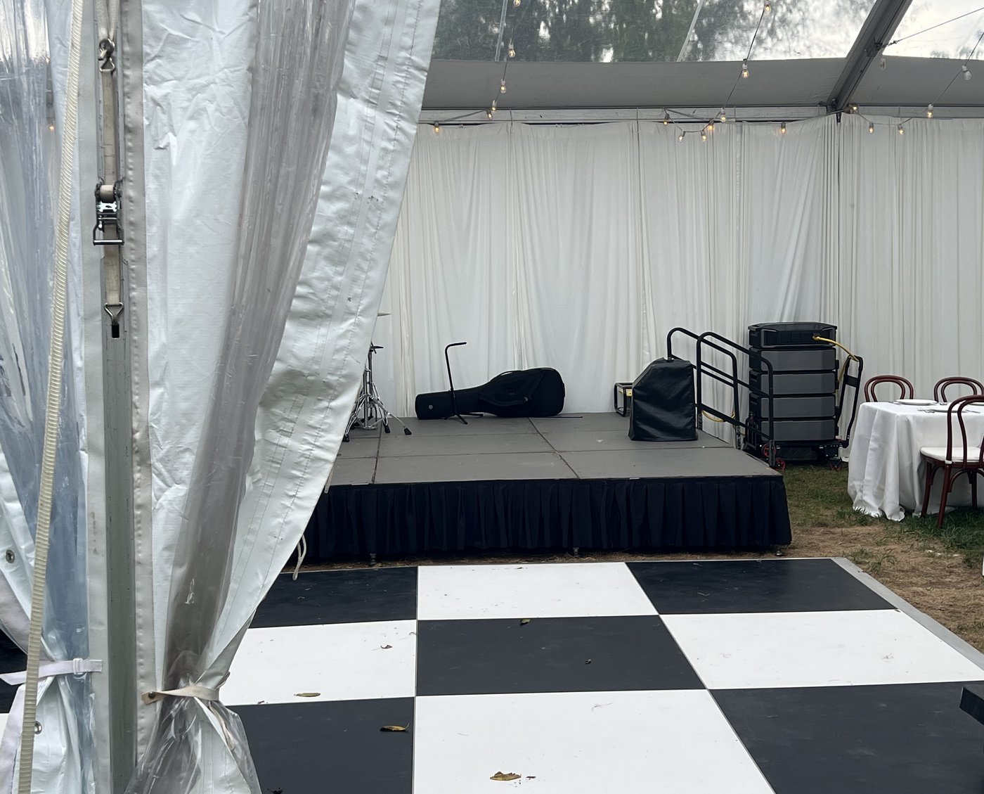 Clear-top wedding tent with a stage, a checkered dance floor, and the silent rig tucked beside the stage rail