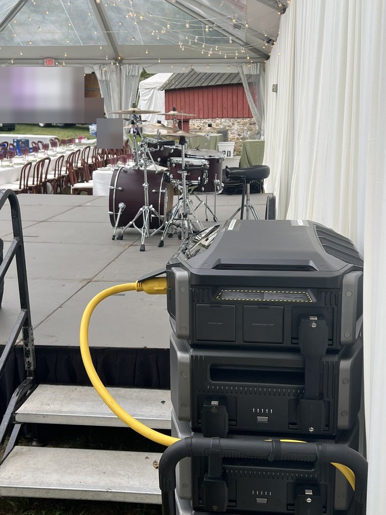 EcoFlow rig at the edge of a wedding tent stage, drum kit and long dining tables behind it